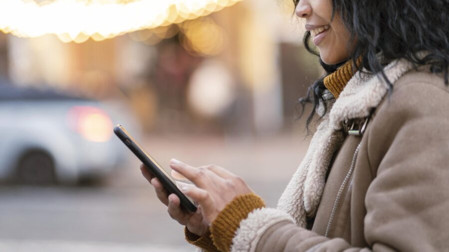 Mulher usando smartphone em ambiente urbano, ilustrando a praticidade do link de autoagendamento para agendar compromissos de forma rápida e fácil.